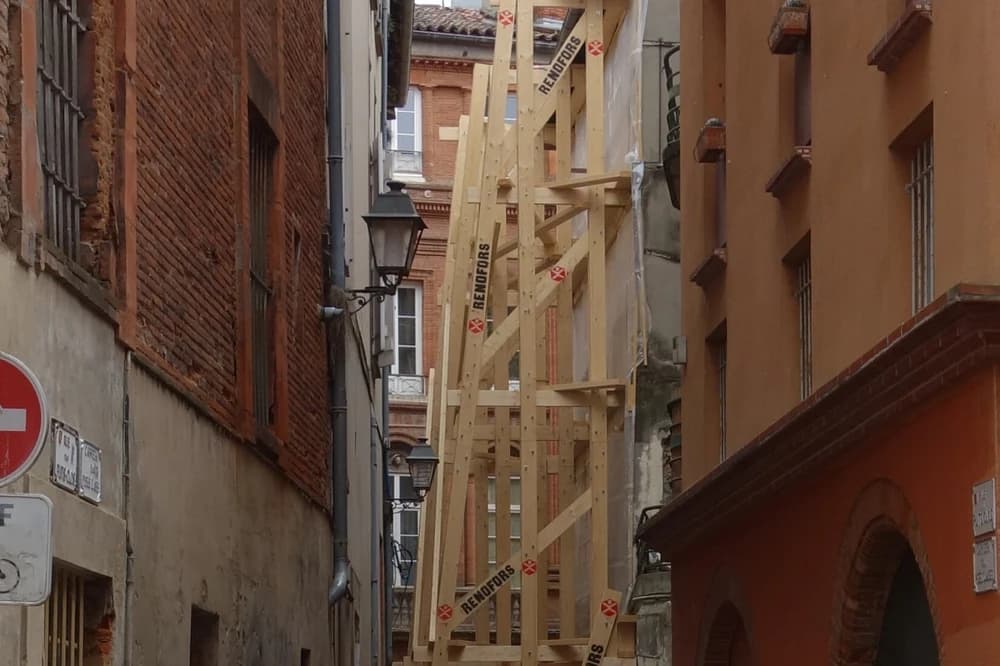 Échafaudage de bois dressé contre une façade de brique, rue des Puits-Clos à Toulouse