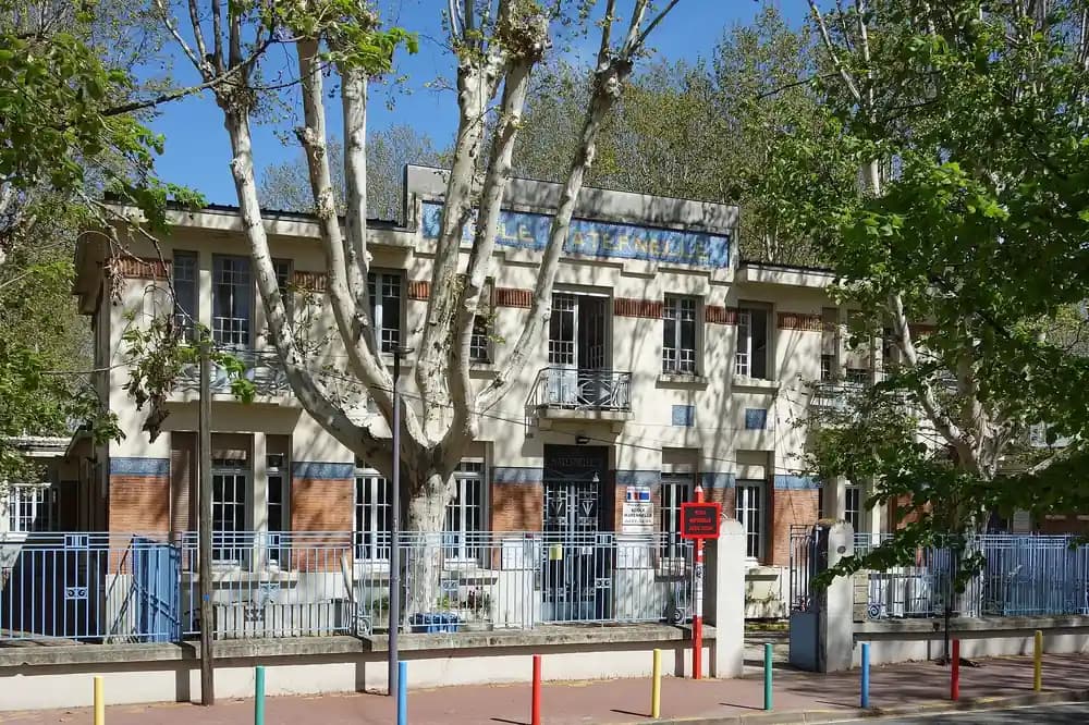 Façade d'une école maternelle de Toulouse derrière ses platanes et sa grille colorée