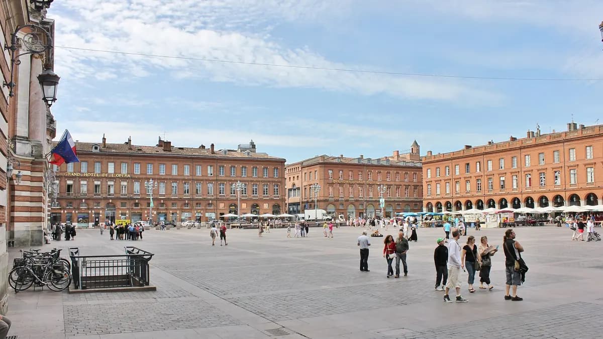 Place du Capitole à Toulouse, façades de brique et passants sous un ciel clair